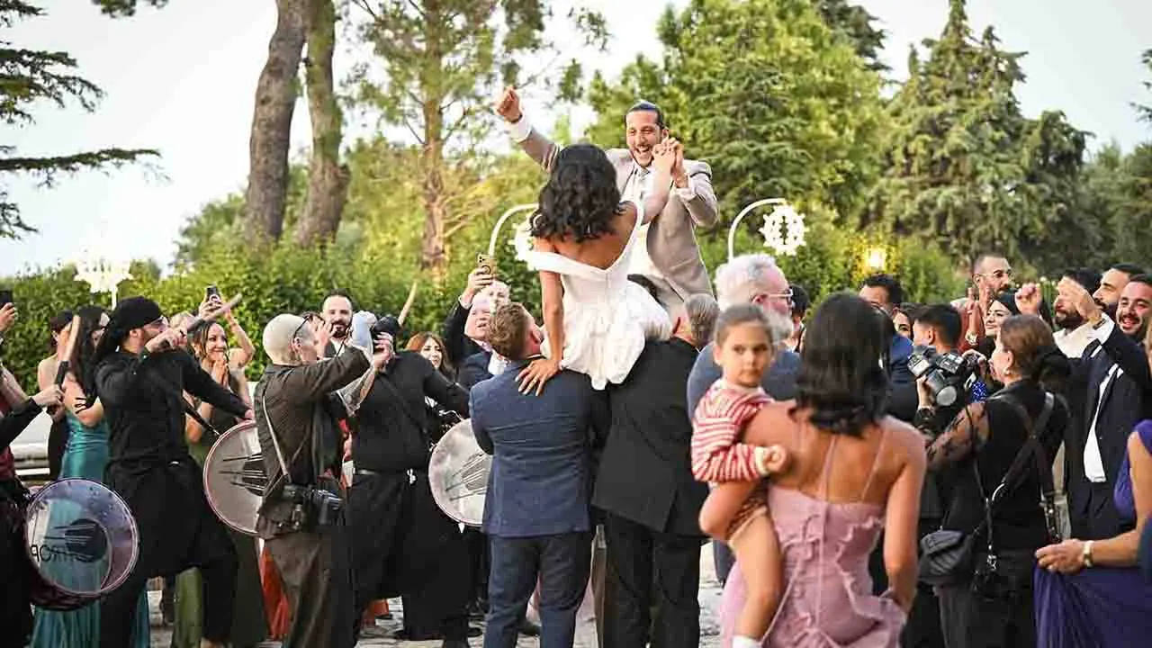 Performance dal vivo di un gruppo di musica Zaffa tradizionale durante l'ingresso degli sposi nella corte interna di una masseria in pietra in Puglia al tramonto.